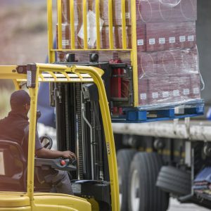 Forklift driver loading pallet onto truck at packaging factory